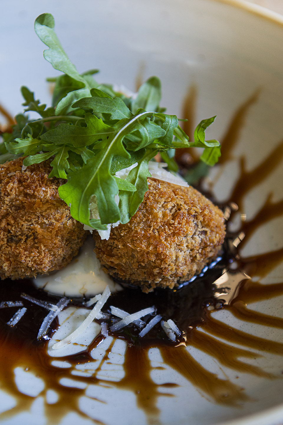 Image shows a close of arancini, balsamic glaze and rocket leaves on a white plate