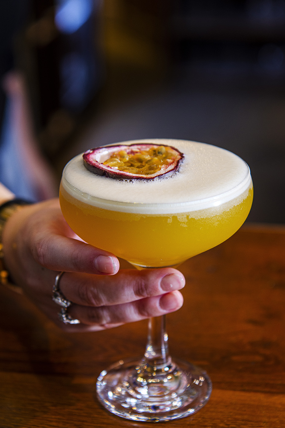 Image shows a close up view of a passion fruit martini with a hand holding the stem of the glass