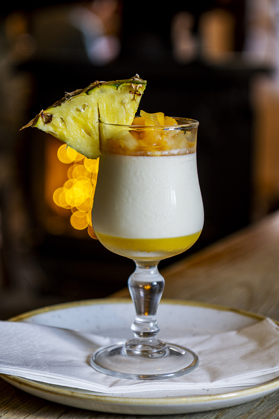 Image shows a close up of a dessert in a tall glass with the slice of pineapple on the rim