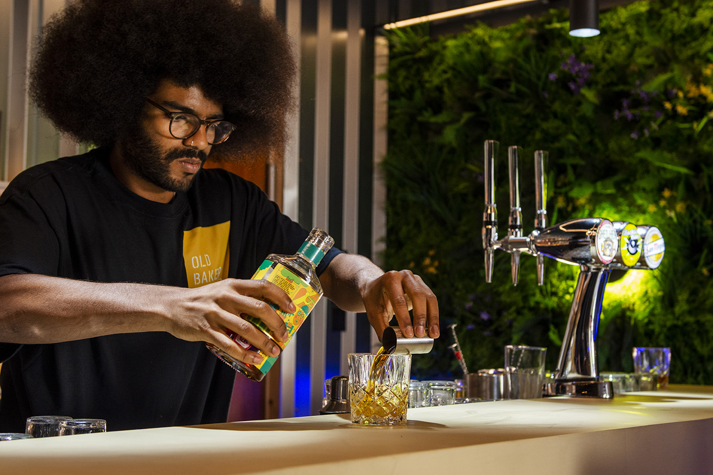 8Track Rum being poured over ice by a barman at The Old Bakery Studios venue, a green plant wall is in the background with atmospheric lighting 