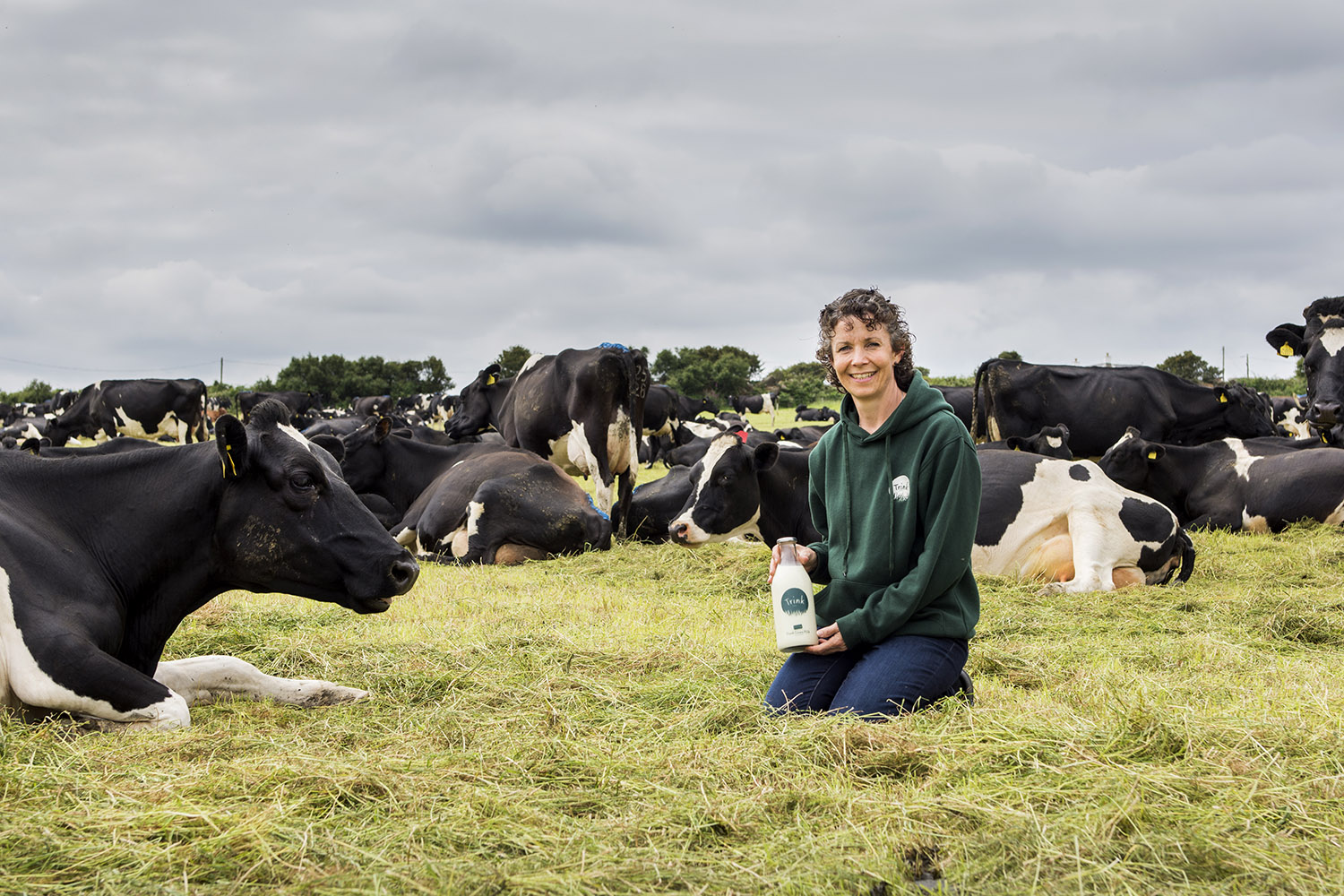 Rachel from Trink Dairy kneeling in a field with a herd of black and white cows around her