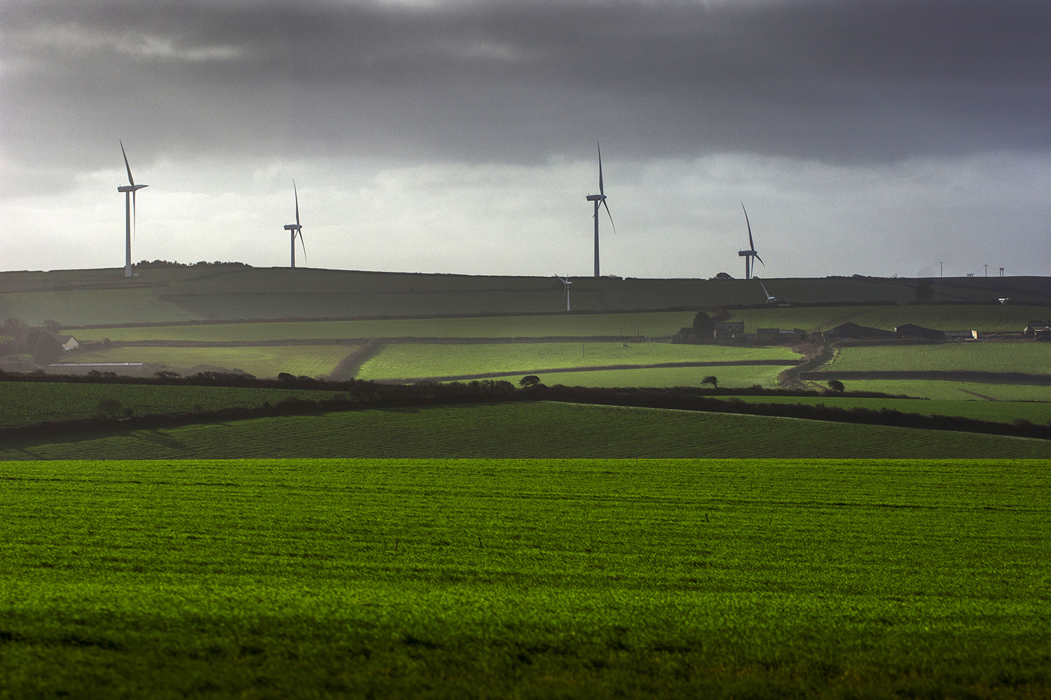 View of wind turbines and rolling green fields on a stormy day in Cornwall