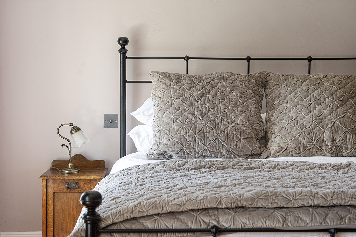 cast iron bed frame with grey quilted throw and cushions on