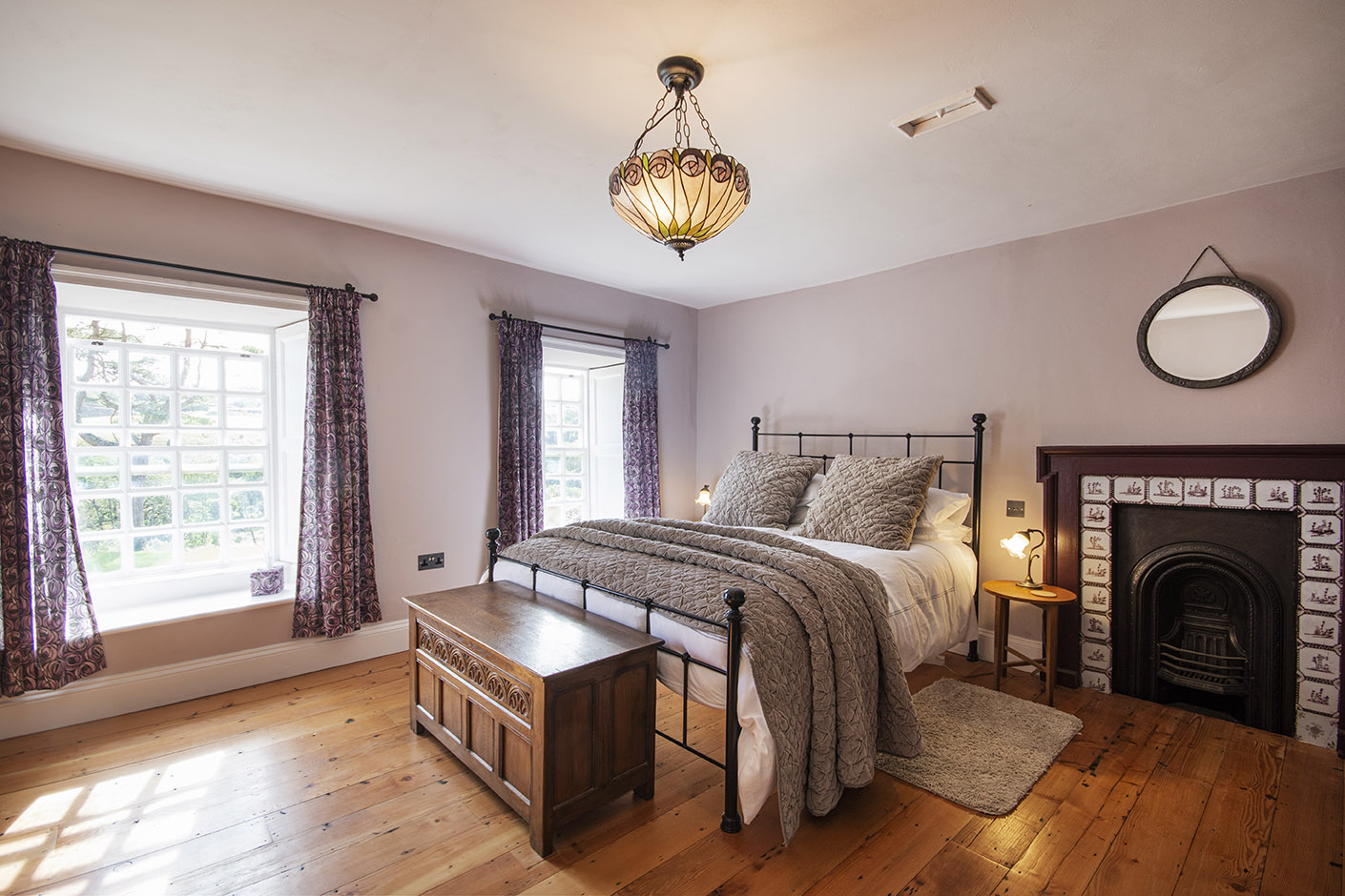 one of the bedrooms decorated in lilac and greys with old fireplace and cast iron bed frame