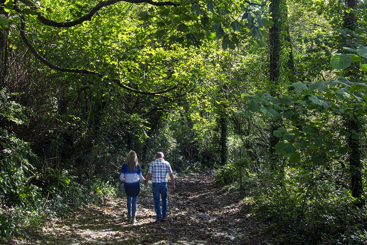 a couple walk down a leafy path through the nature reserve in summer time