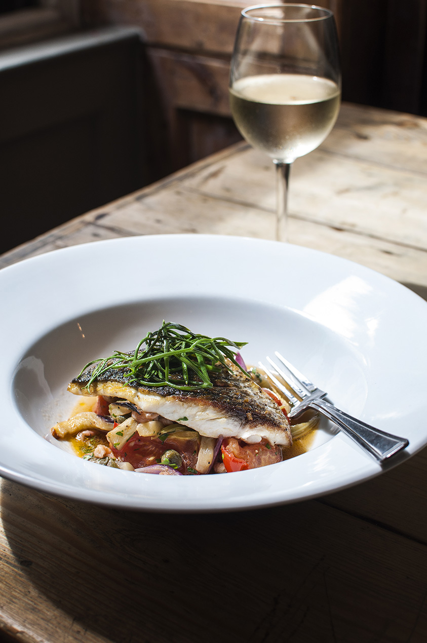 Photo of a plate of mullet with samphire on the top and a glass of chilled white wine in the background at the Queens Hotel in St Ives.