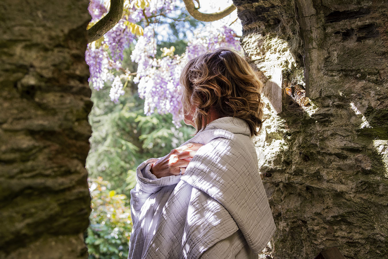 model wraps herself in a throw whilst standing in an old stone doorway at Caerhays Castle with lots of beautiful wisteria in the background