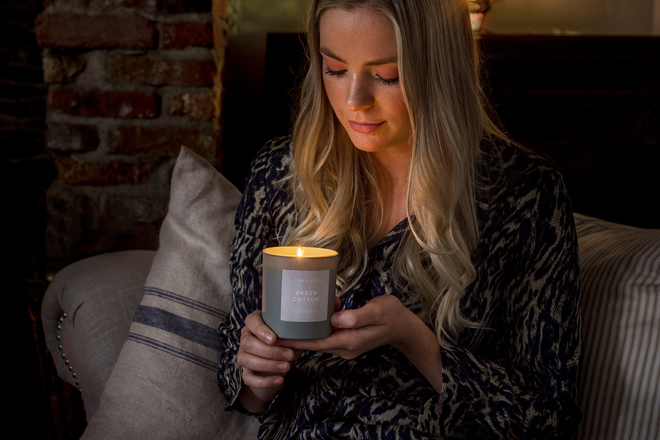 female model holds a lit scented candle in a darkened room