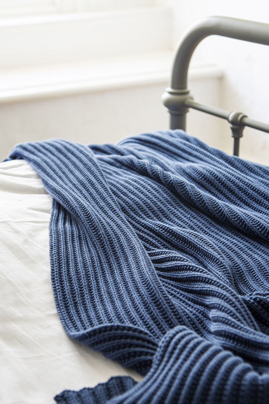 a textured blue throw on a metal bed with white linens 