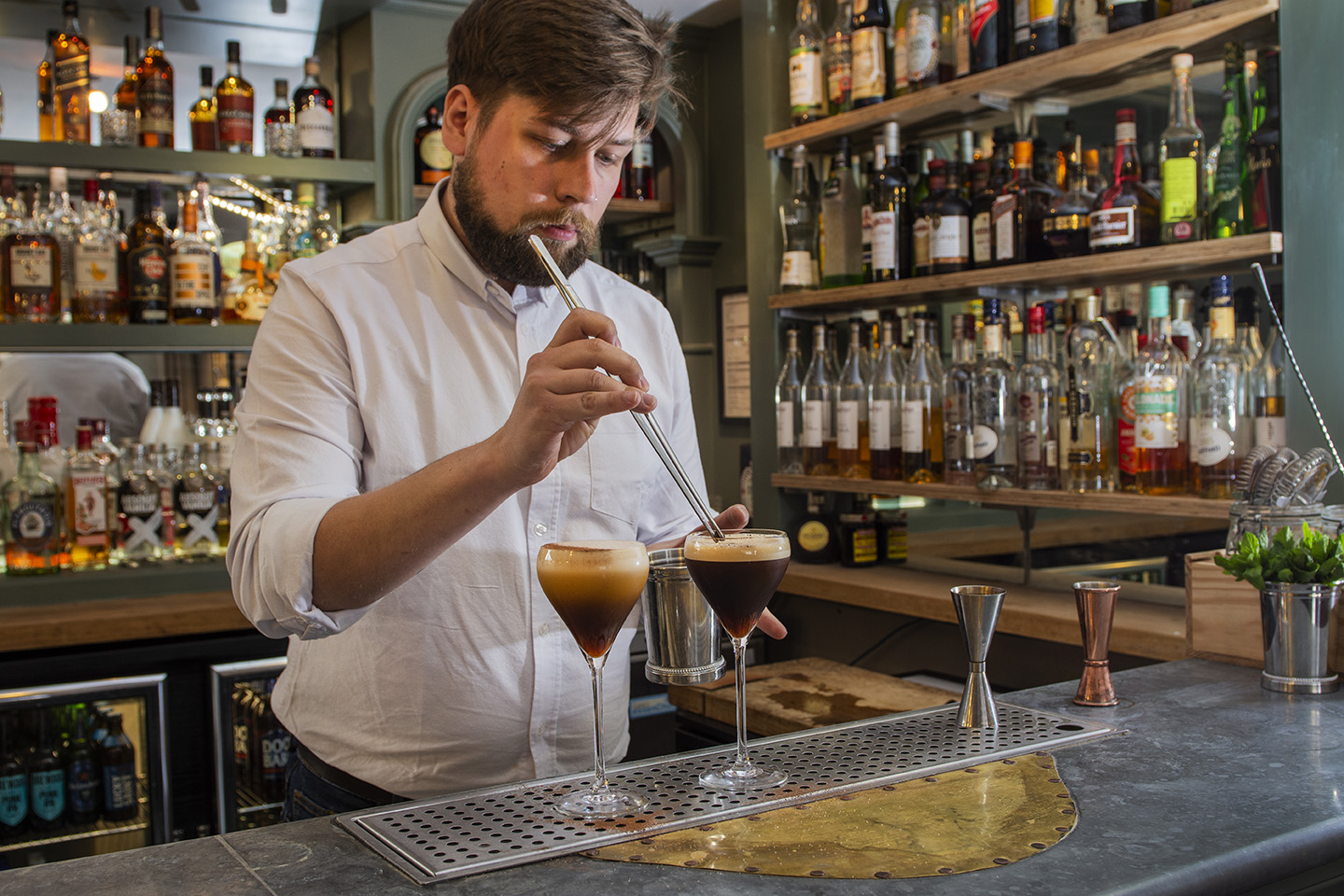 A barman uses tweezers to add a coffee bean finishing touch to an Espresso Martini cocktail 