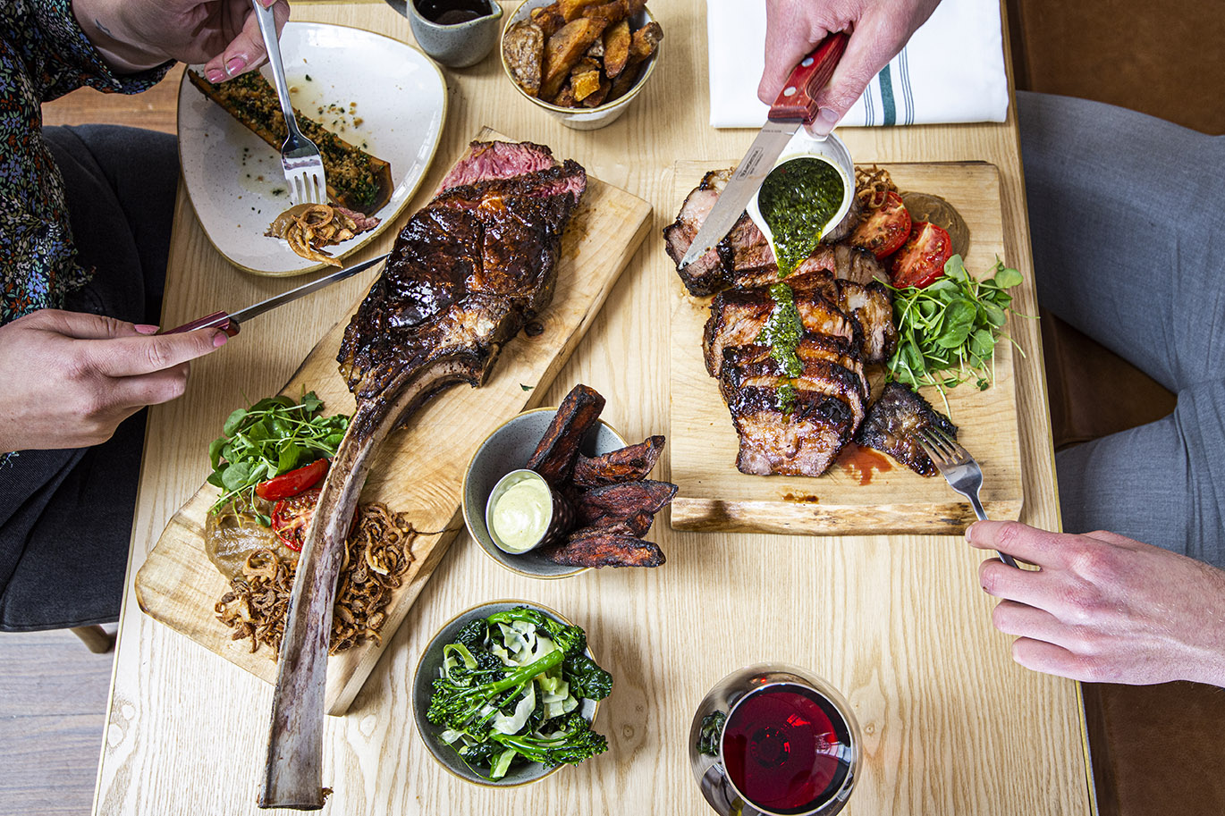 An overhead view of a large tomahawk steak and various other plates of food with a couple dining at the table 