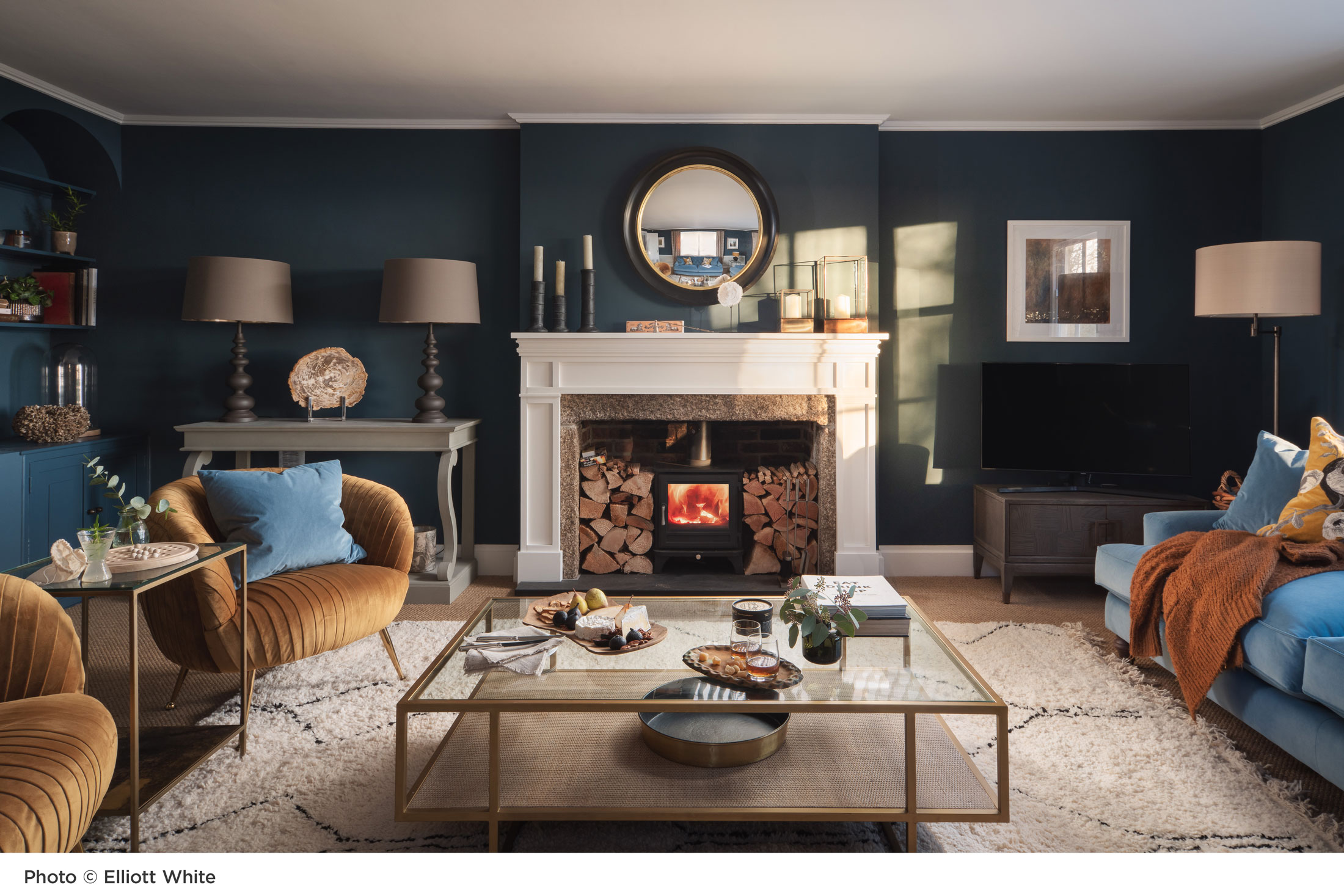 photo of a lounge designed by Nicola decorated in blues and golds with a log burner at the centre