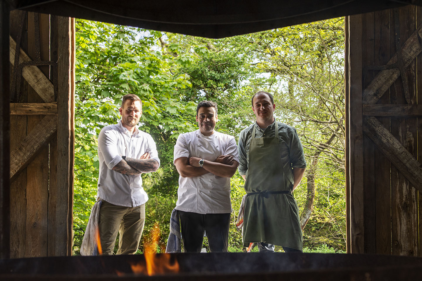 Three chefs including Paul Ainsworth and Jackson Bristow in a large barn doorway at Nancarrow Farm with fire in the foreground