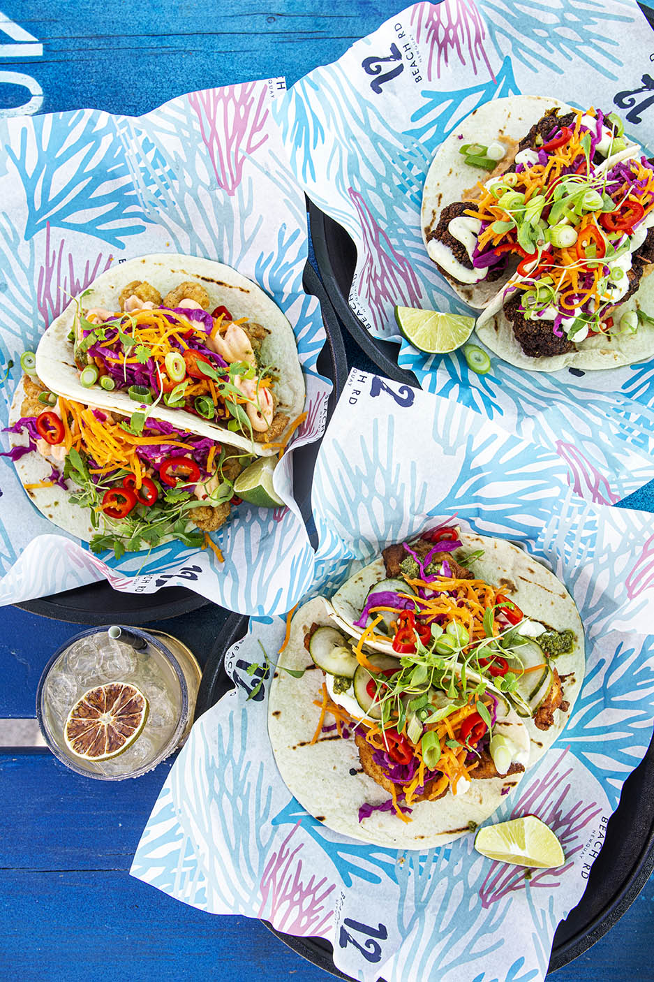 Overhead view of three plates of colourful tacos on a blue wooden background