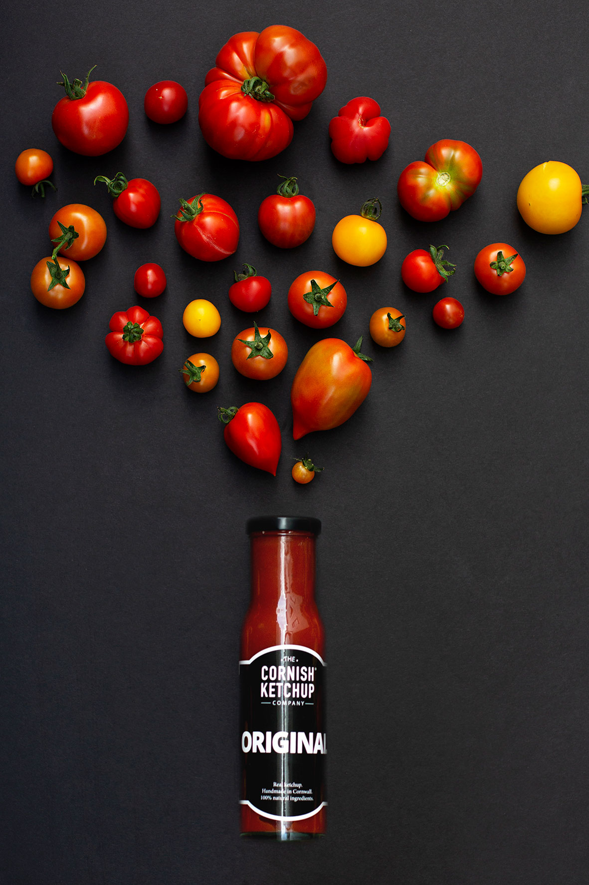 artistic photo of heritage tomatoes arranged above a bottle of ketchup on a black background