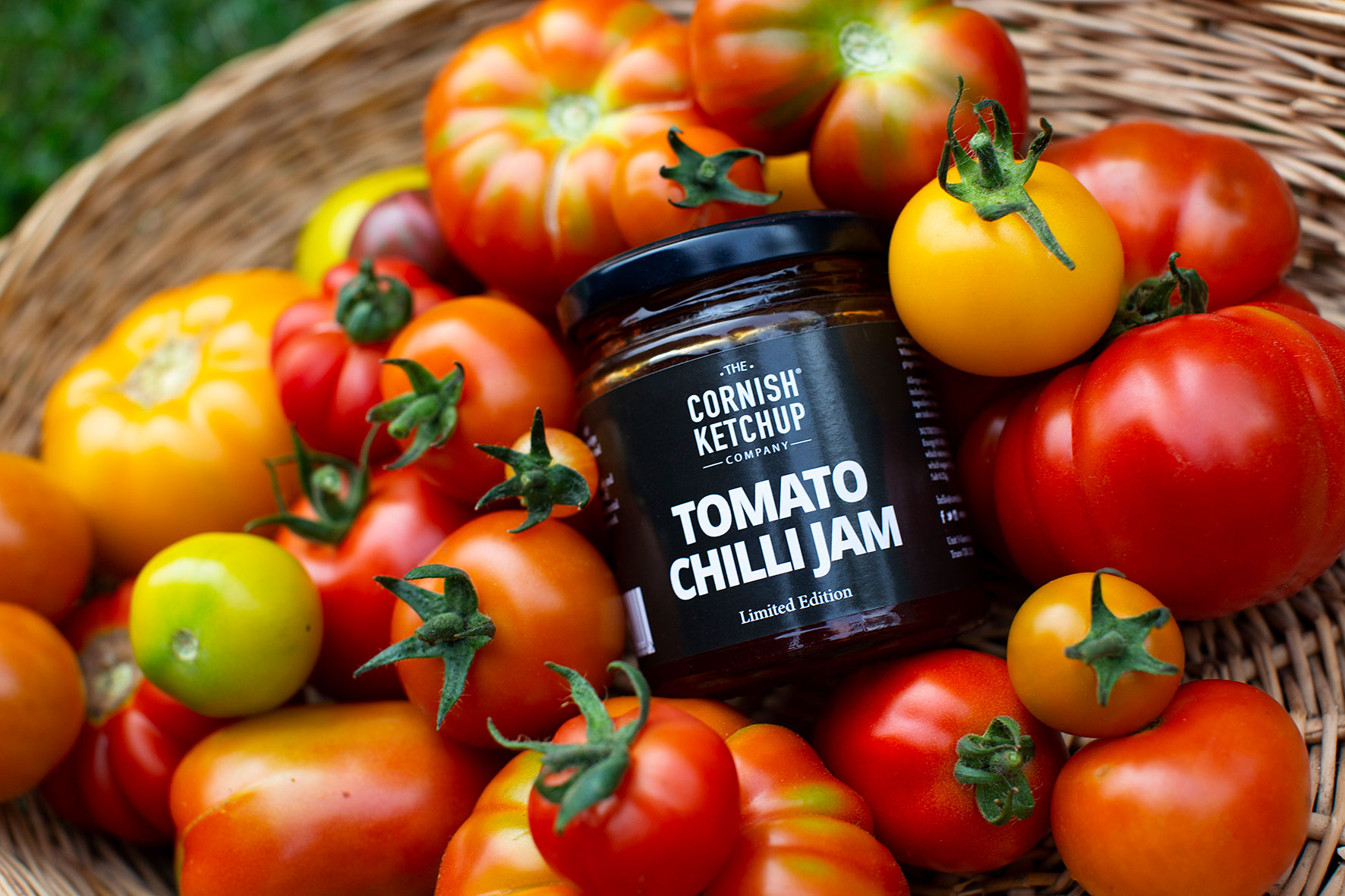 jar of tomato chilli jam in a basket of red and yellow tomatoes