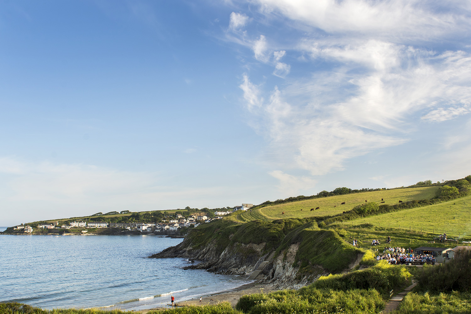 View of the Hidden Hut, Porthcurnick beach and coastline stretching around to Portscatho on a sunny evening