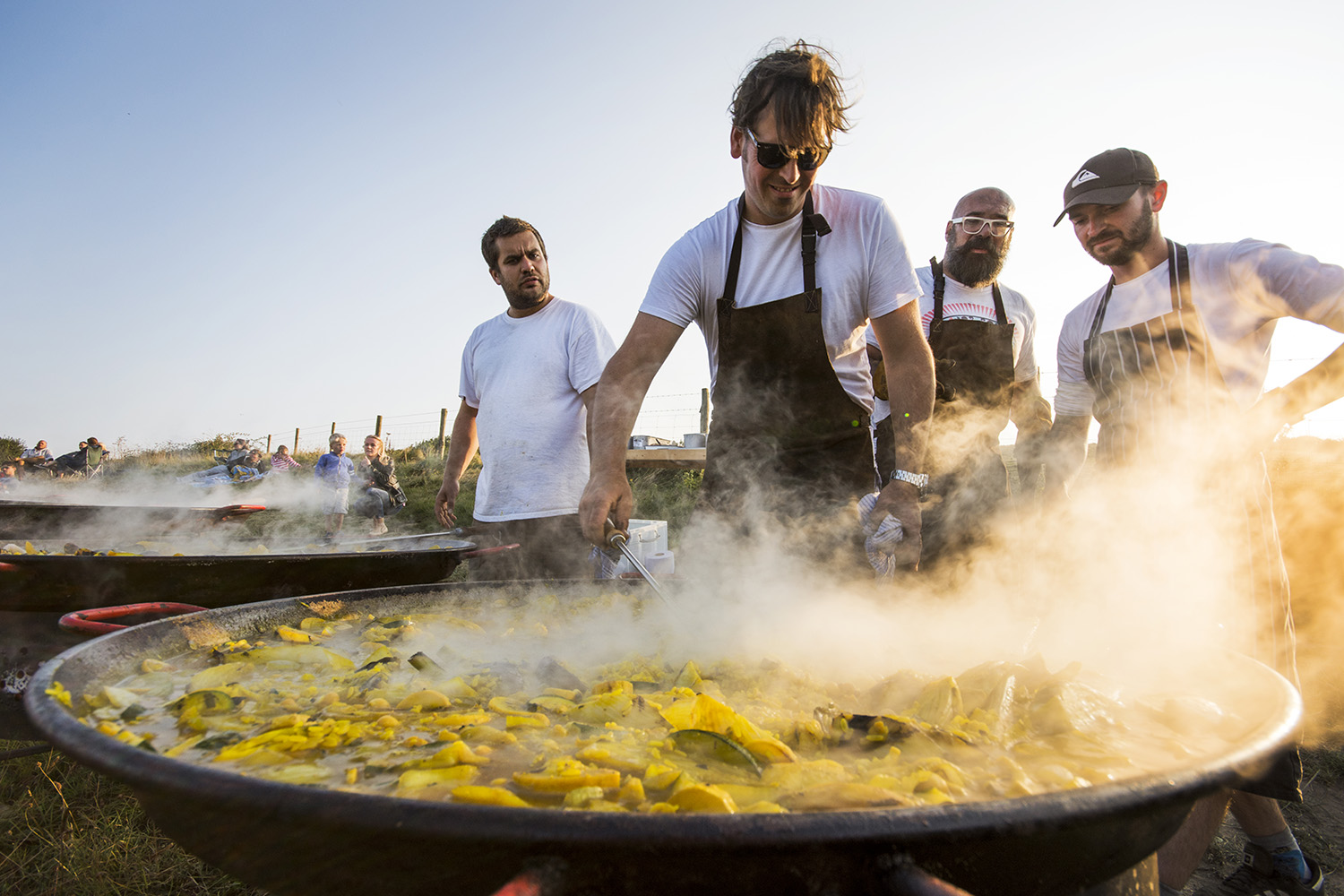 Simon Stallard stirring up a huge pan of paella with Hidden Hut chefs looking on 